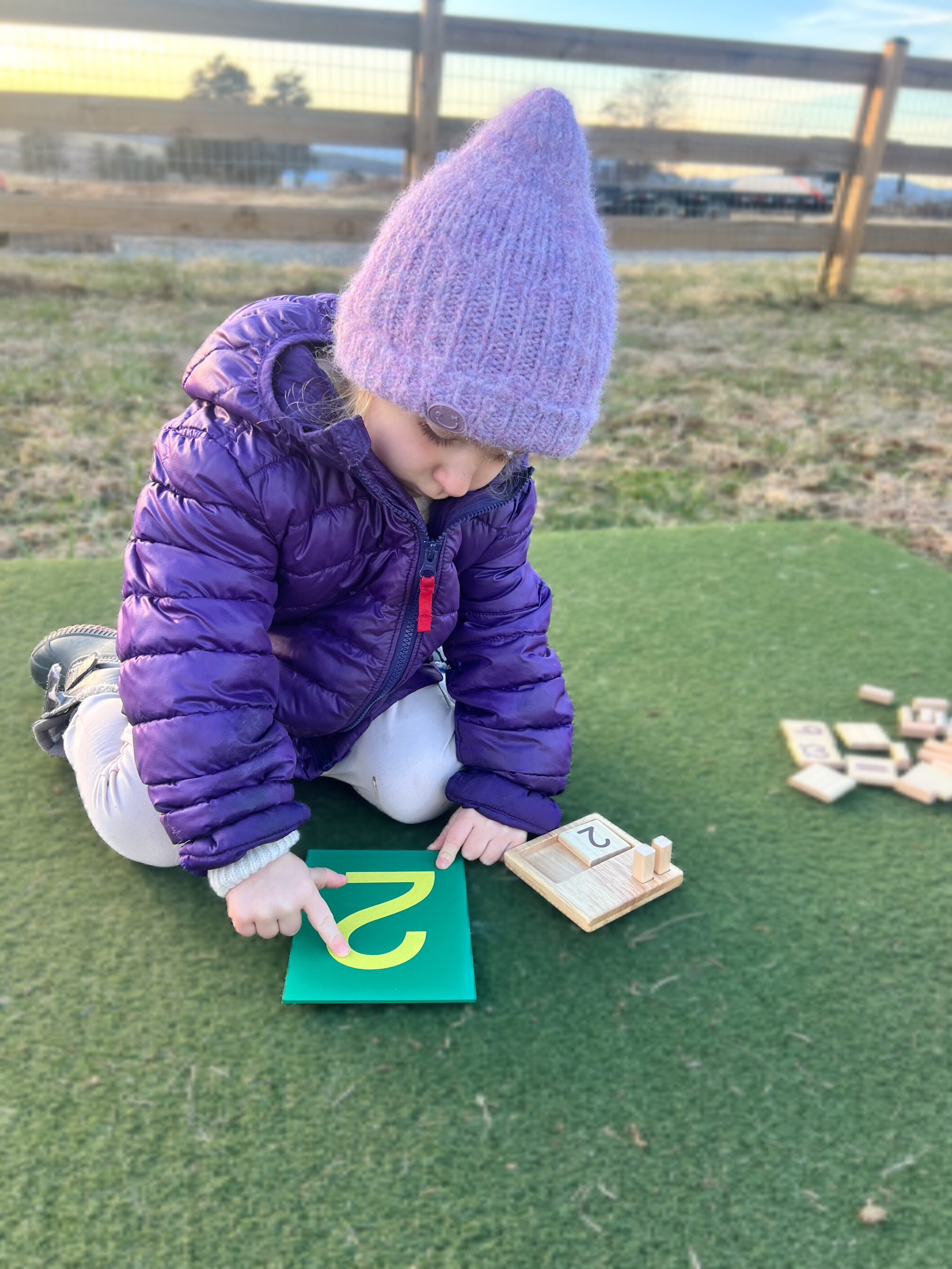 Small child sitting on the ground learning how to draw the number 2 by tracing a printout of the number