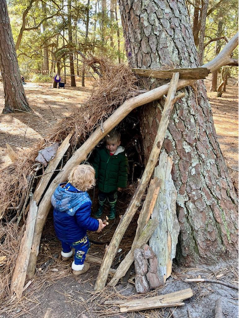 Two little children interacting and exploring a nature shelter built in the woods
