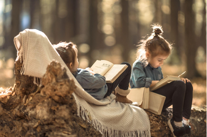 Two little girls sitting on a log reading books in an autumn forest