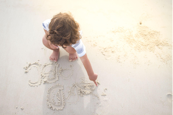 Little child tracing letters of the alphabet in the sand on a beach